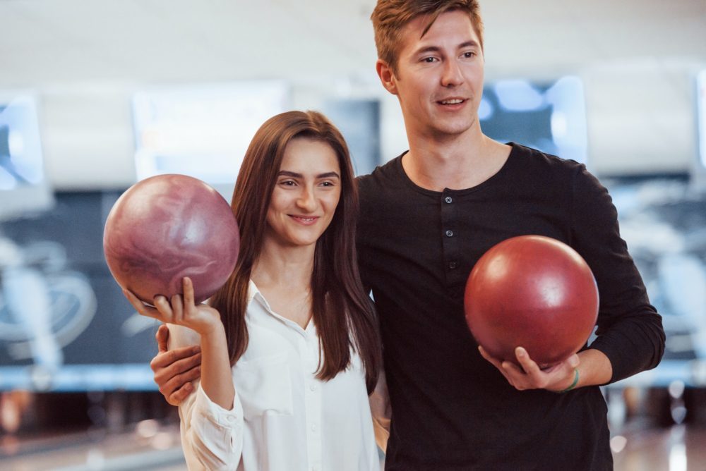 Happy couple holding bowling balls in hands and have good time in the club
