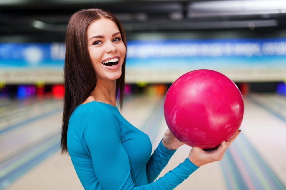 My lucky ball. Beautiful young women holding a bowling ball while standing against bowling alleys