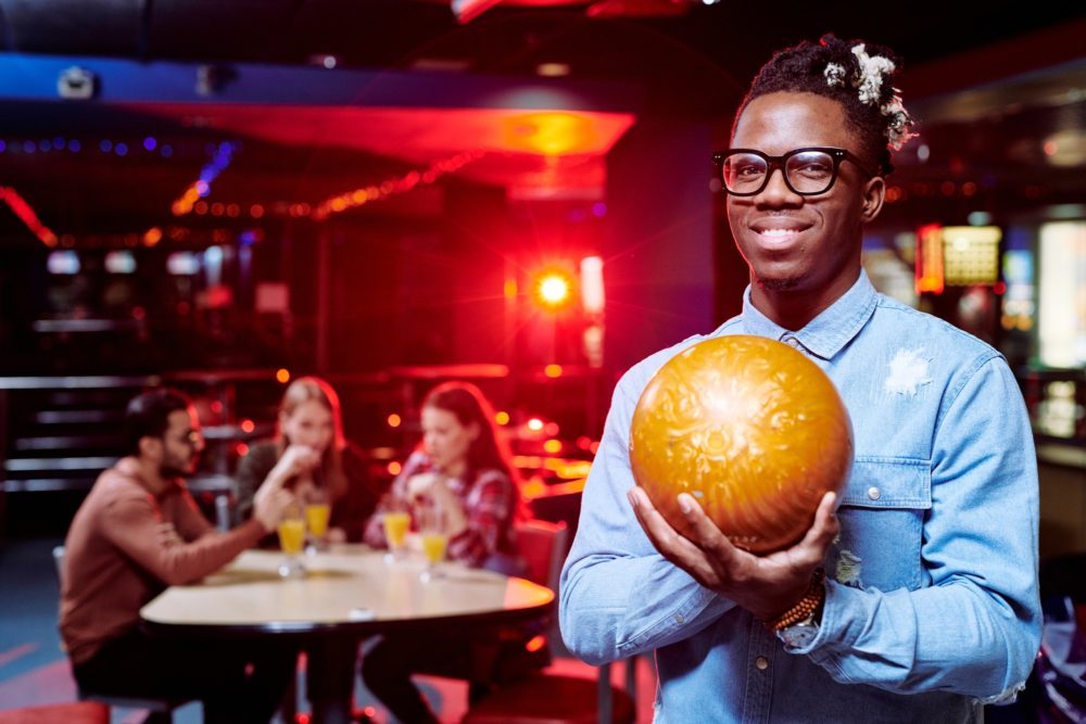 Happy young African man with bowling ball standing in front of camera